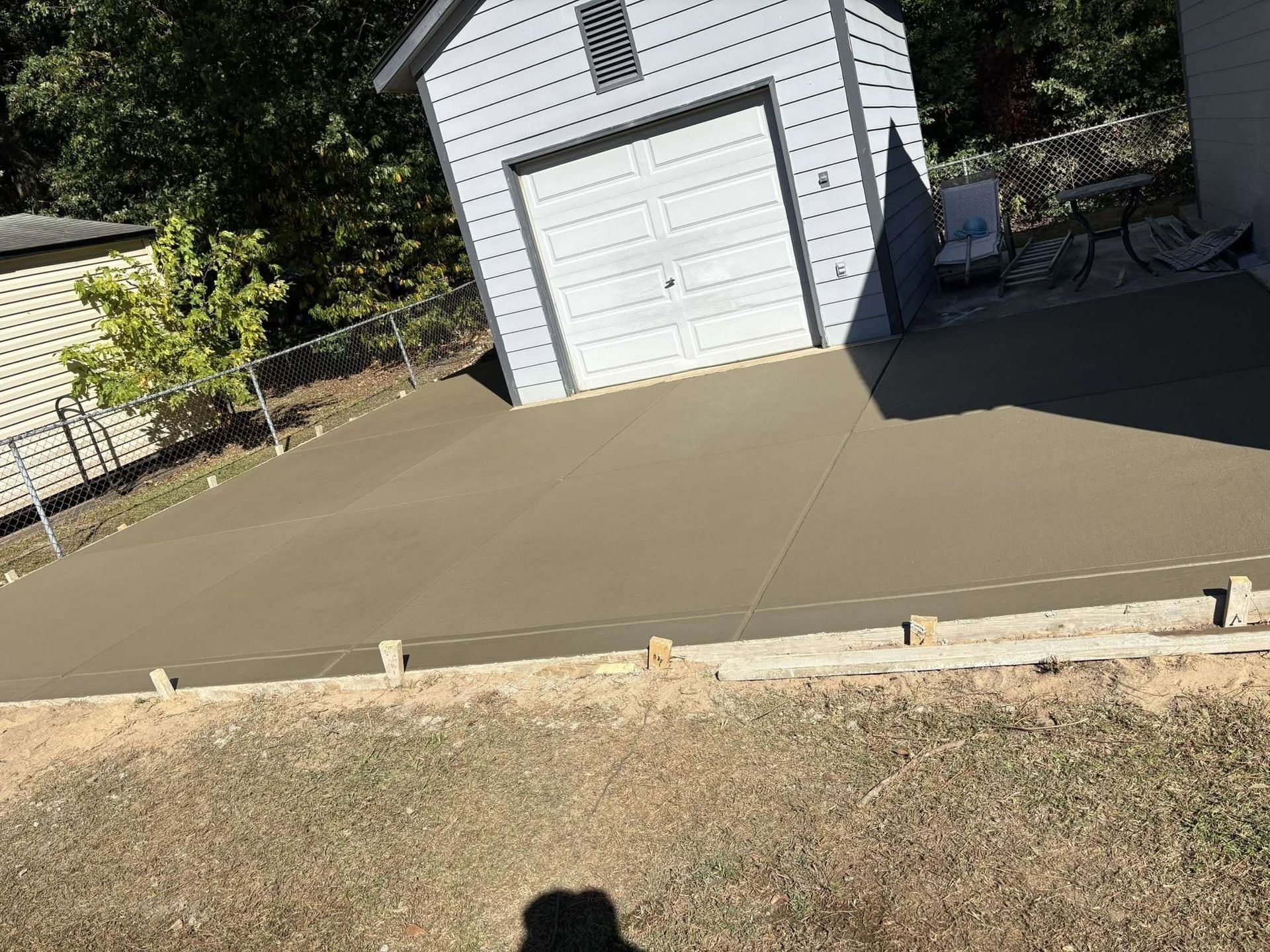 Fresh concrete patio/driveway slab in front of a white garage with surrounding dirt and grass