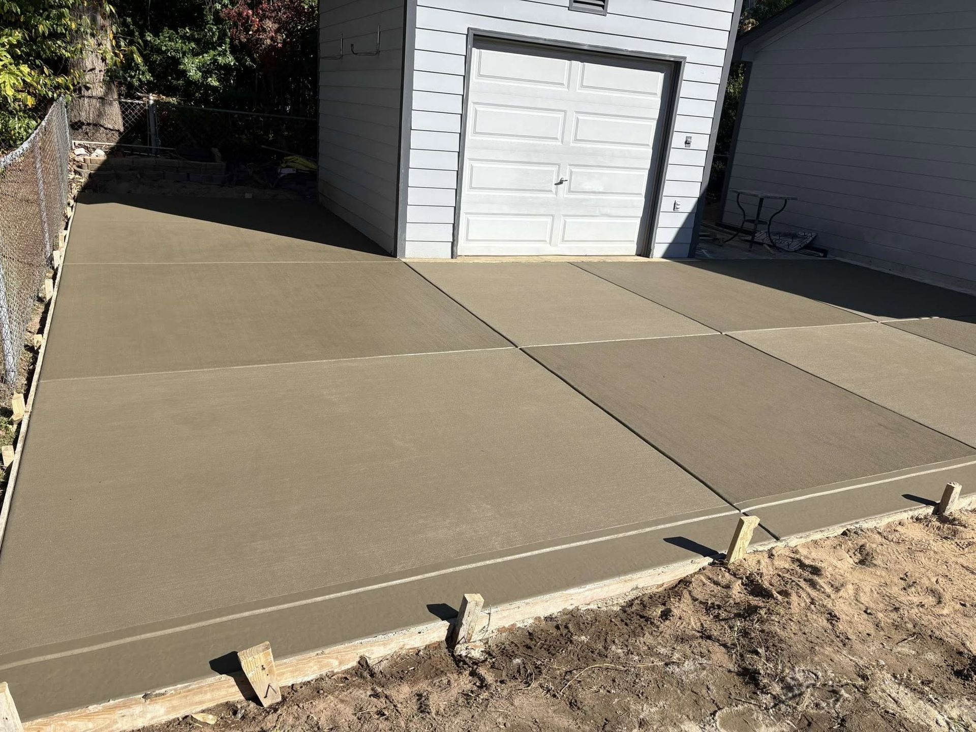Freshly poured concrete driveway beside a white garage, with wooden forms along the edge.