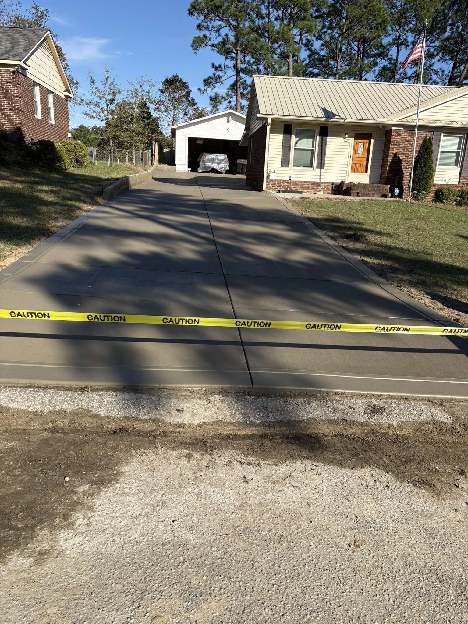 Residential driveway blocked by yellow caution tape near a house and garage on a sunny day