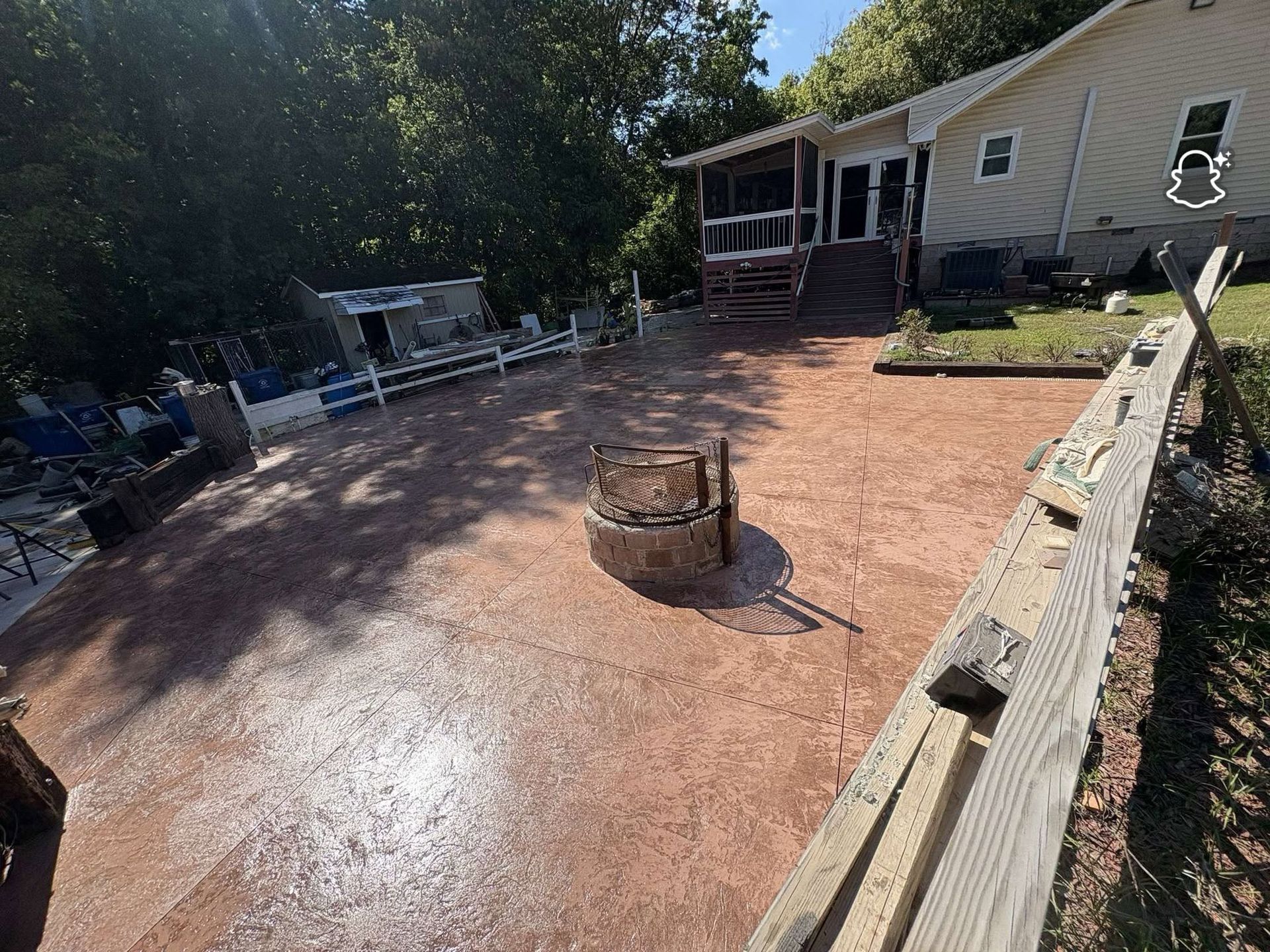 Backyard patio with wet red concrete, fire pit in center, and house with deck in the background