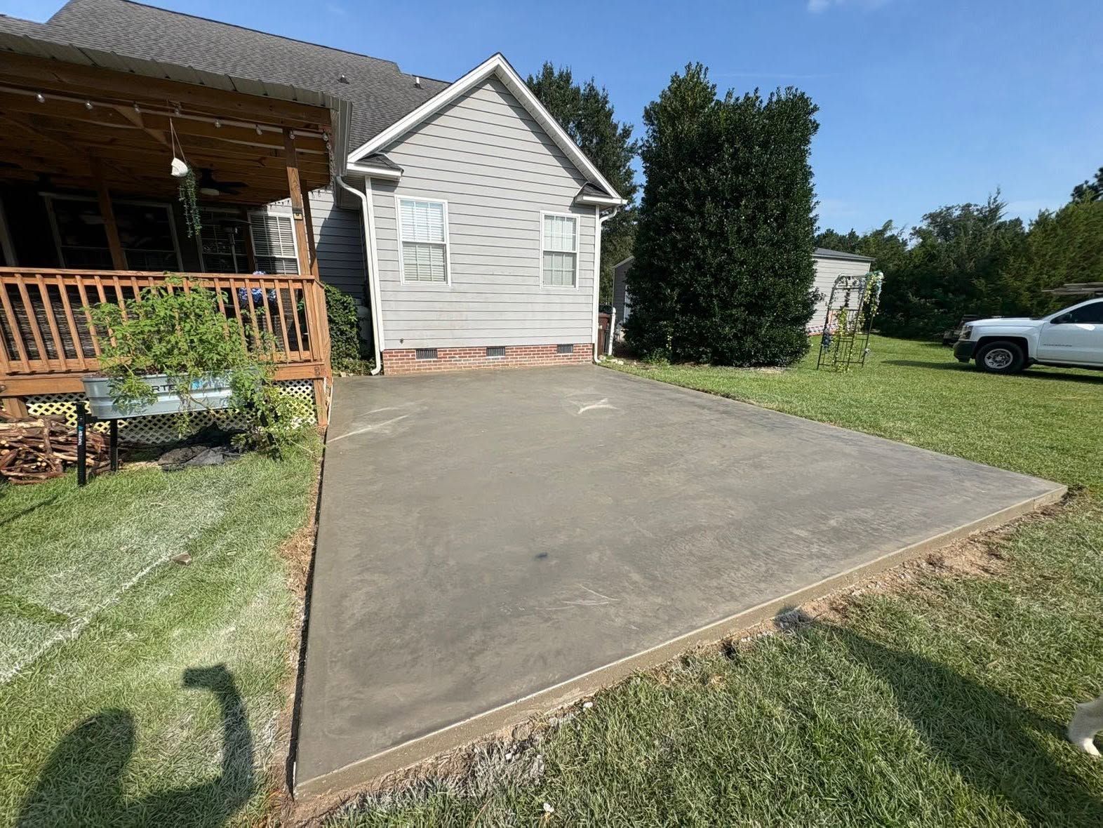 Concrete driveway beside a house with wooden deck, grass yard, and parked white truck in the background
