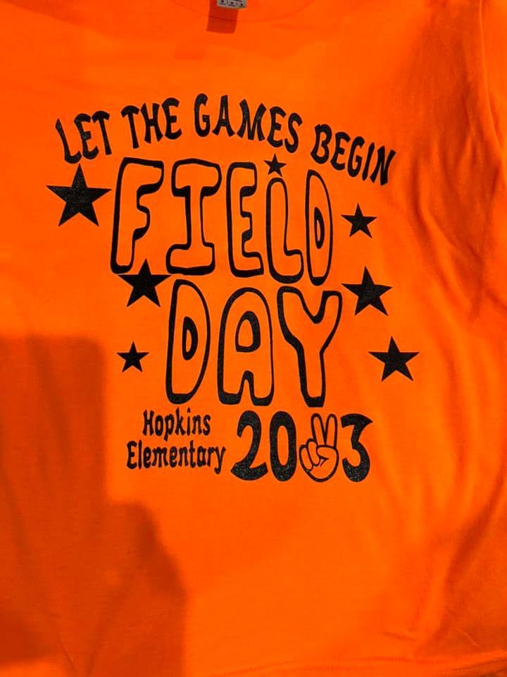 Bright orange Hopkins Elementary Field Day 2023 t-shirt with black text featuring stars and a peace sign.