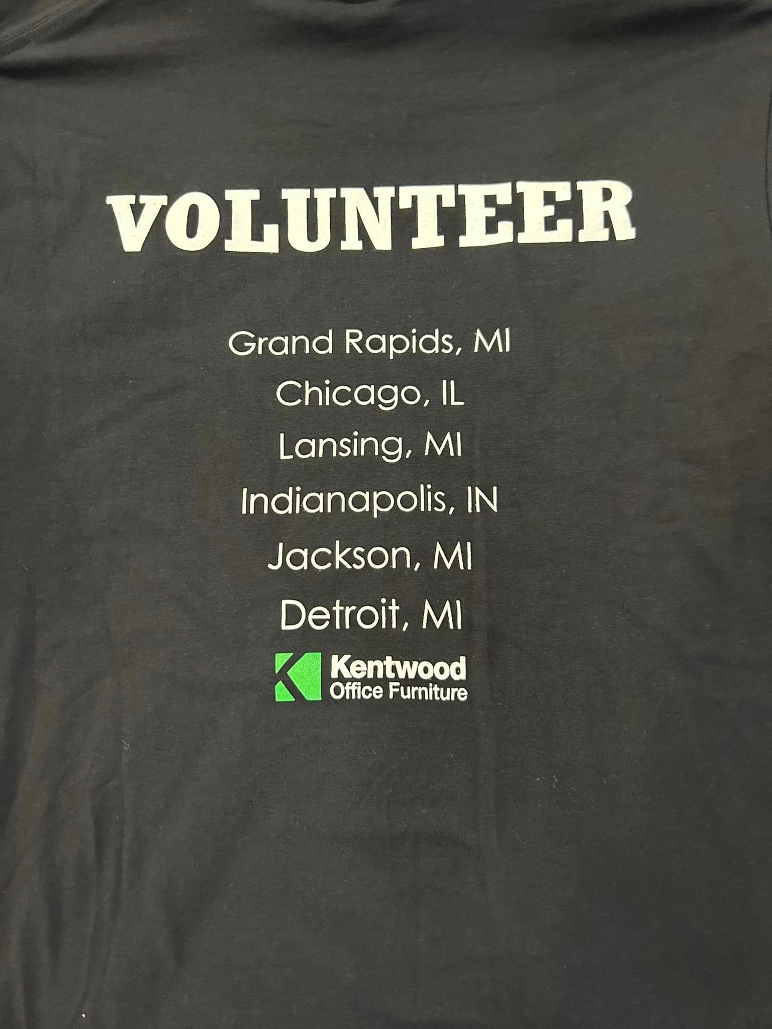 Black volunteer t-shirt listing cities: Grand Rapids, Chicago, Lansing, Indianapolis, Jackson, Detroit; Kentwood logo below.