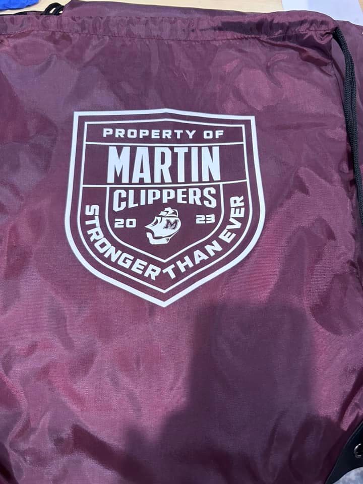 A maroon drawstring bag featuring a white shield logo that reads