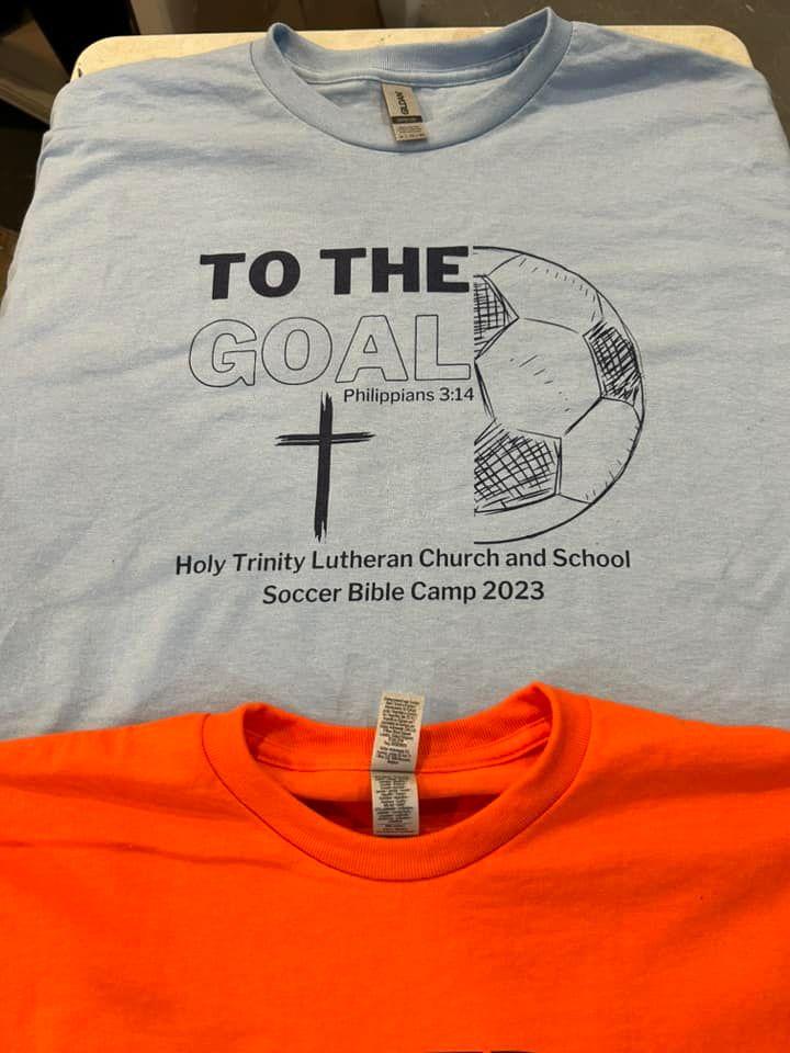 A light blue shirt with a soccer ball and cross graphic above