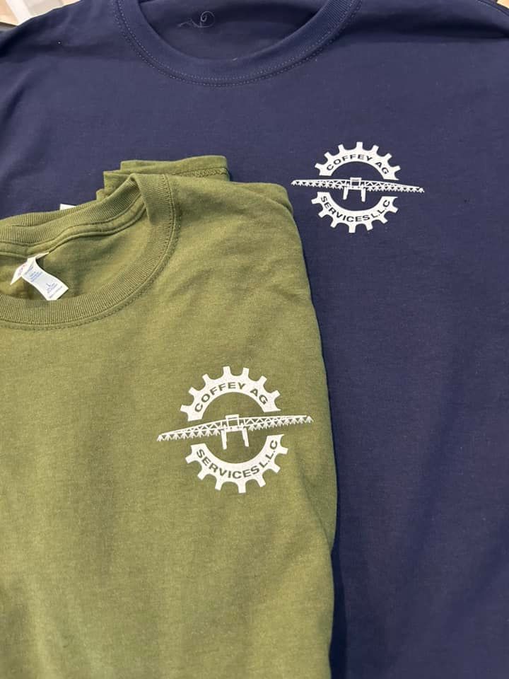 An olive green t-shirt and a dark blue t-shirt, both featuring a white logo of a gear surrounding an agricultural sprayer.