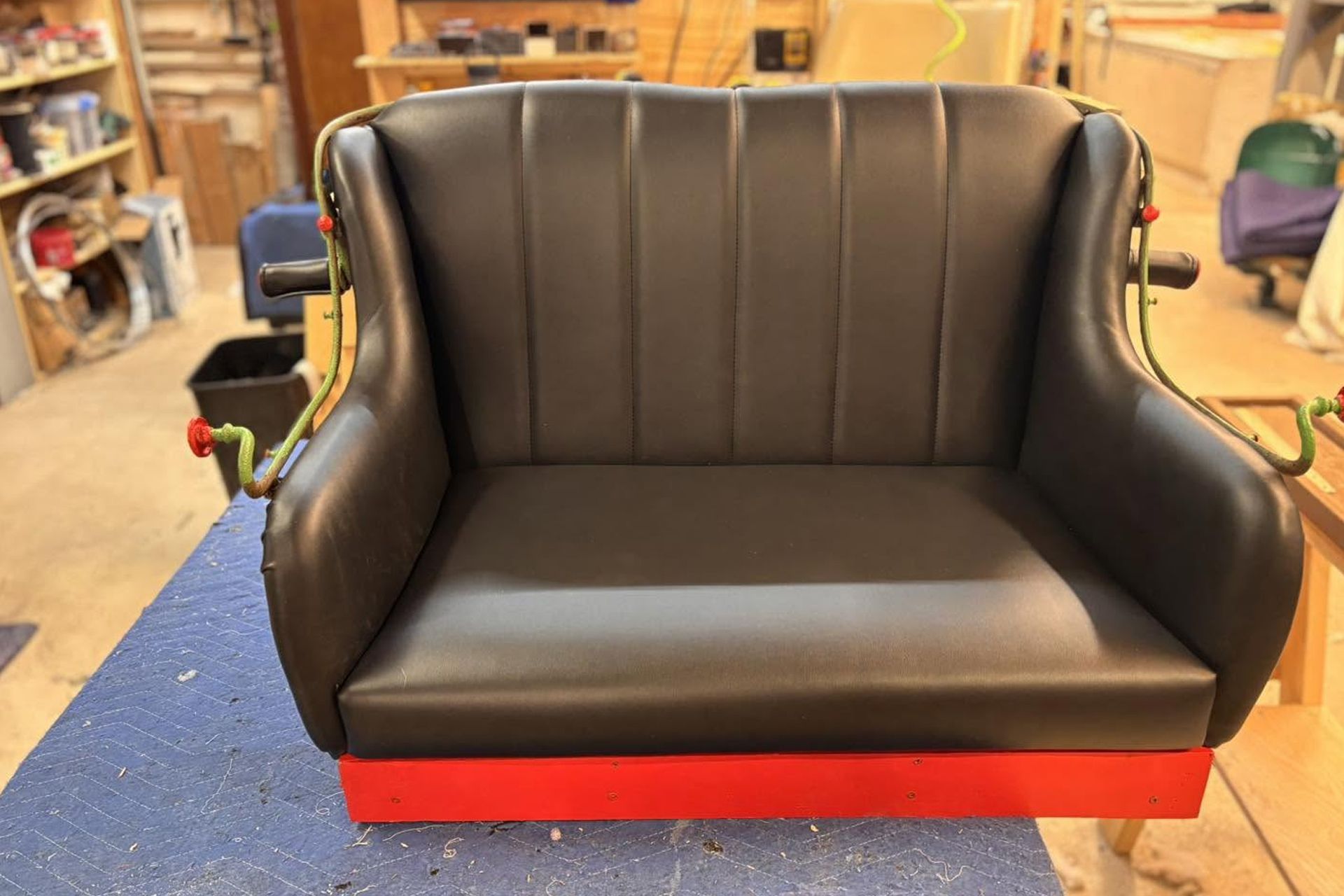 Black upholstered bench seat with red base in a workshop or garage setting