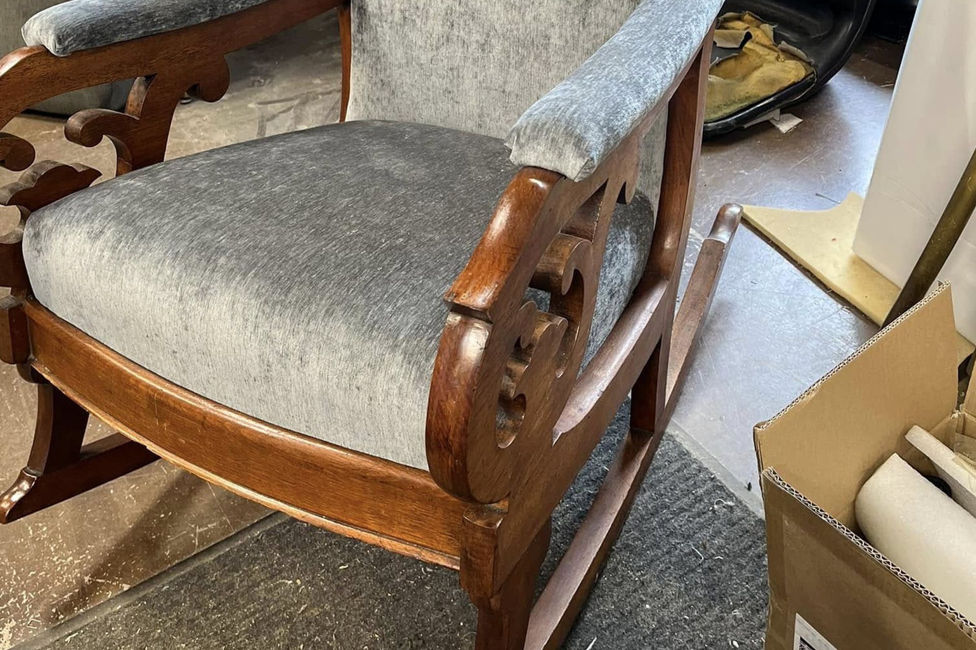Wooden armchair with gray cushions in a cluttered room near cardboard boxes