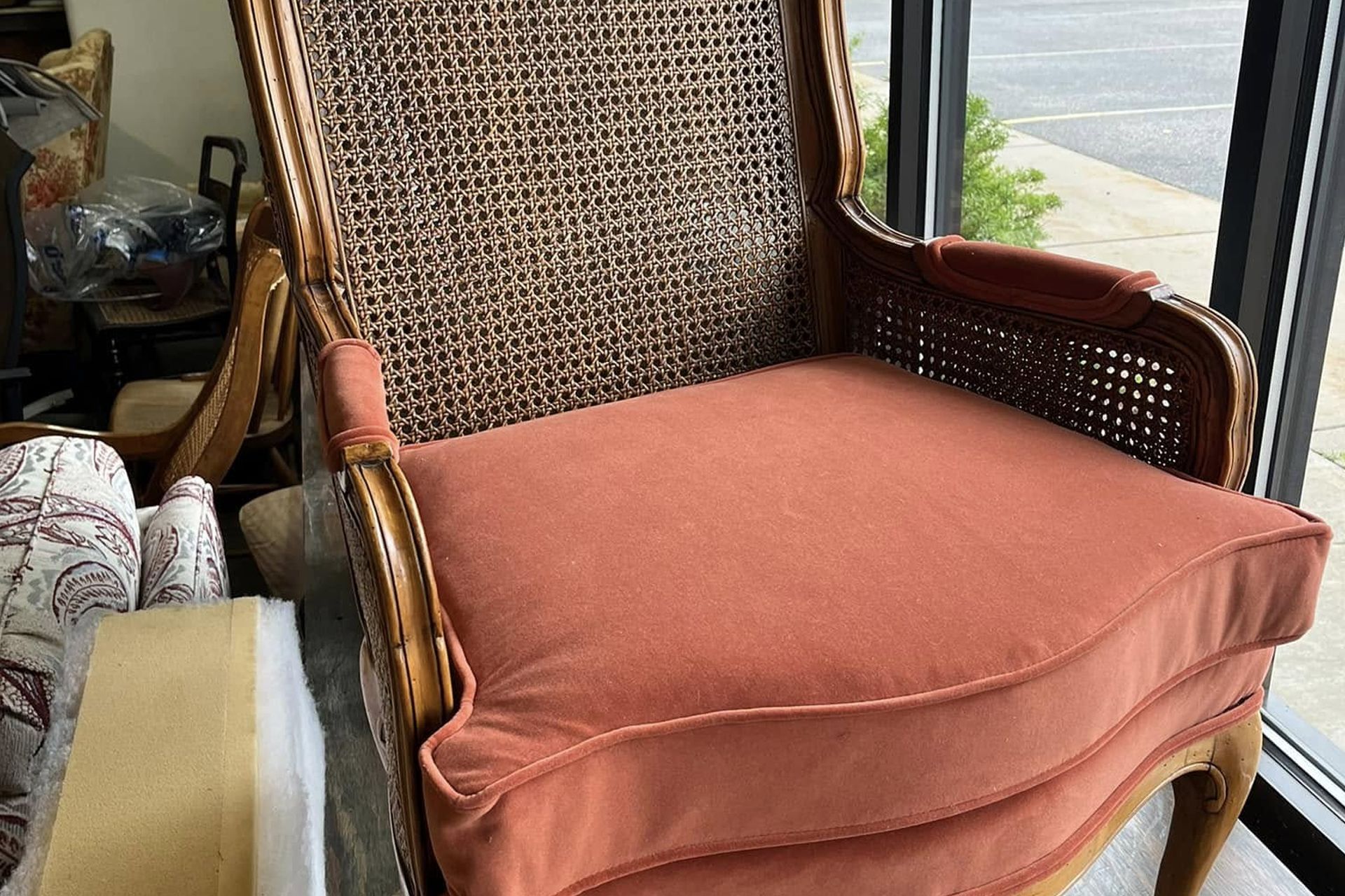 Wicker armchair with rust-colored cushion by a window, with a folded blanket beside it.