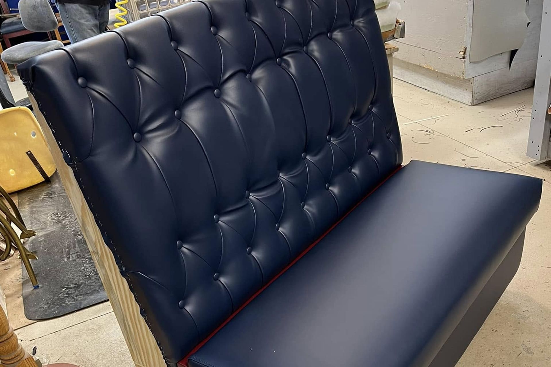 Blue tufted upholstered bench with a high back in a showroom or workshop setting