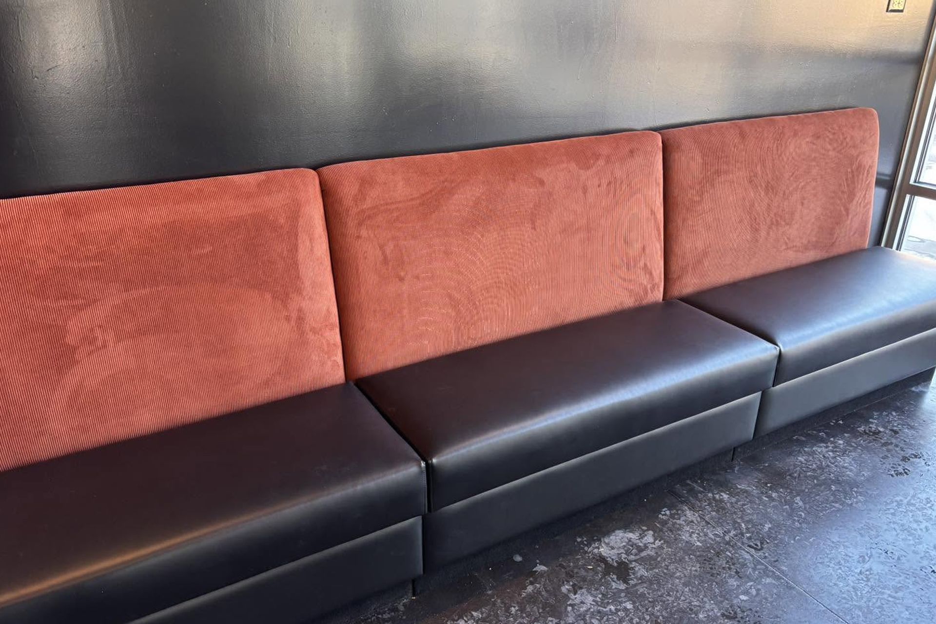 Three-seat black leather couch with rust-orange textured cushions against a dark wall.