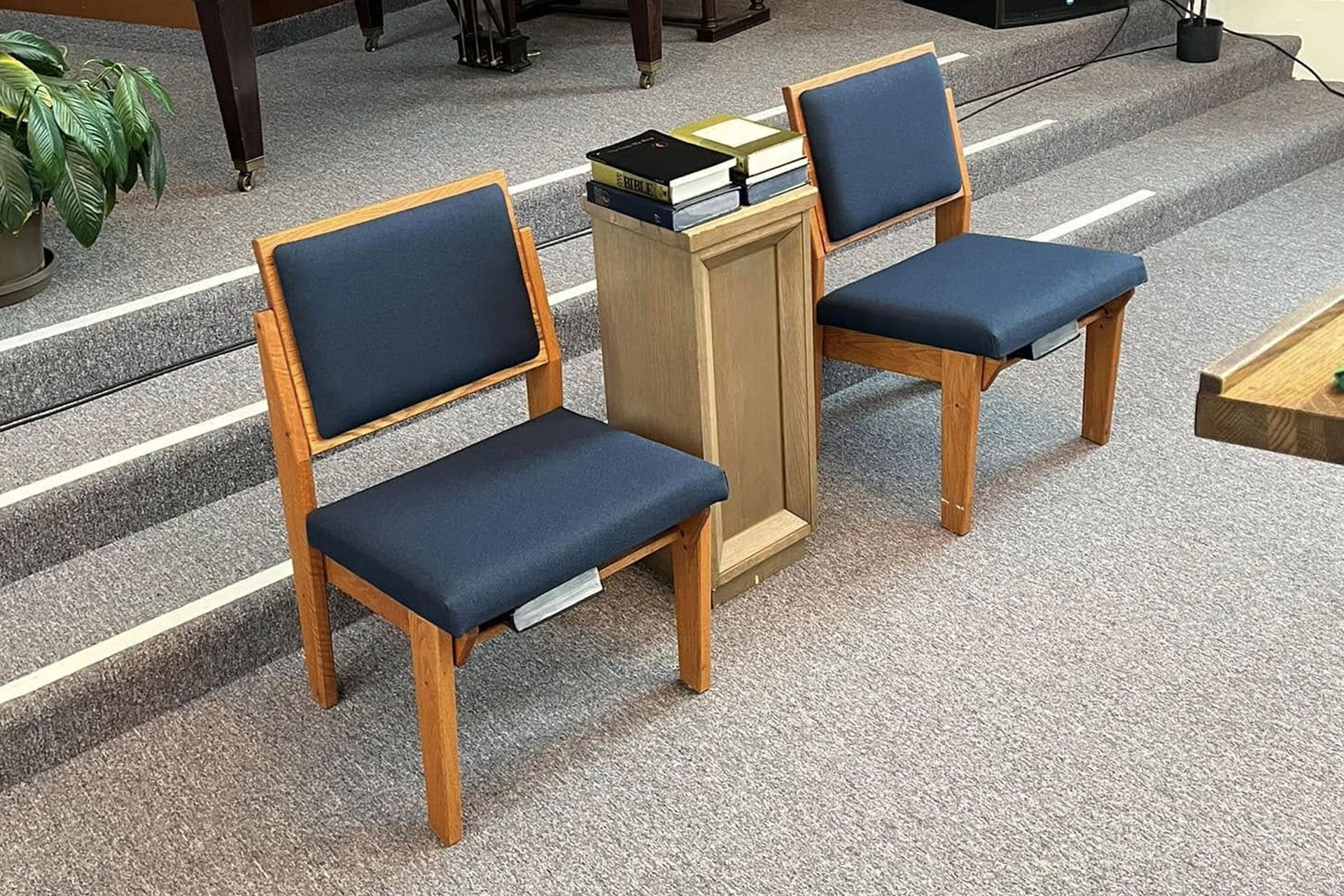 Two blue upholstered chairs beside a wooden offering stand in a church interior