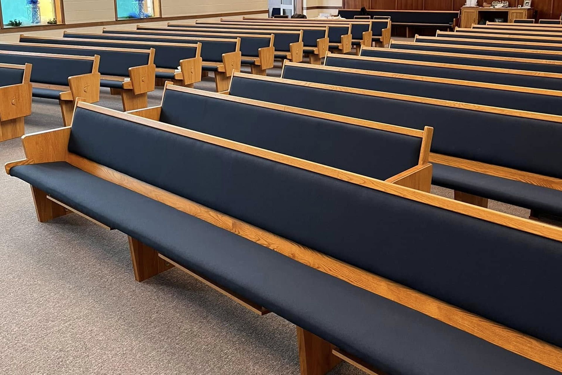 Rows of empty wooden church pews with dark blue cushions in a sanctuary