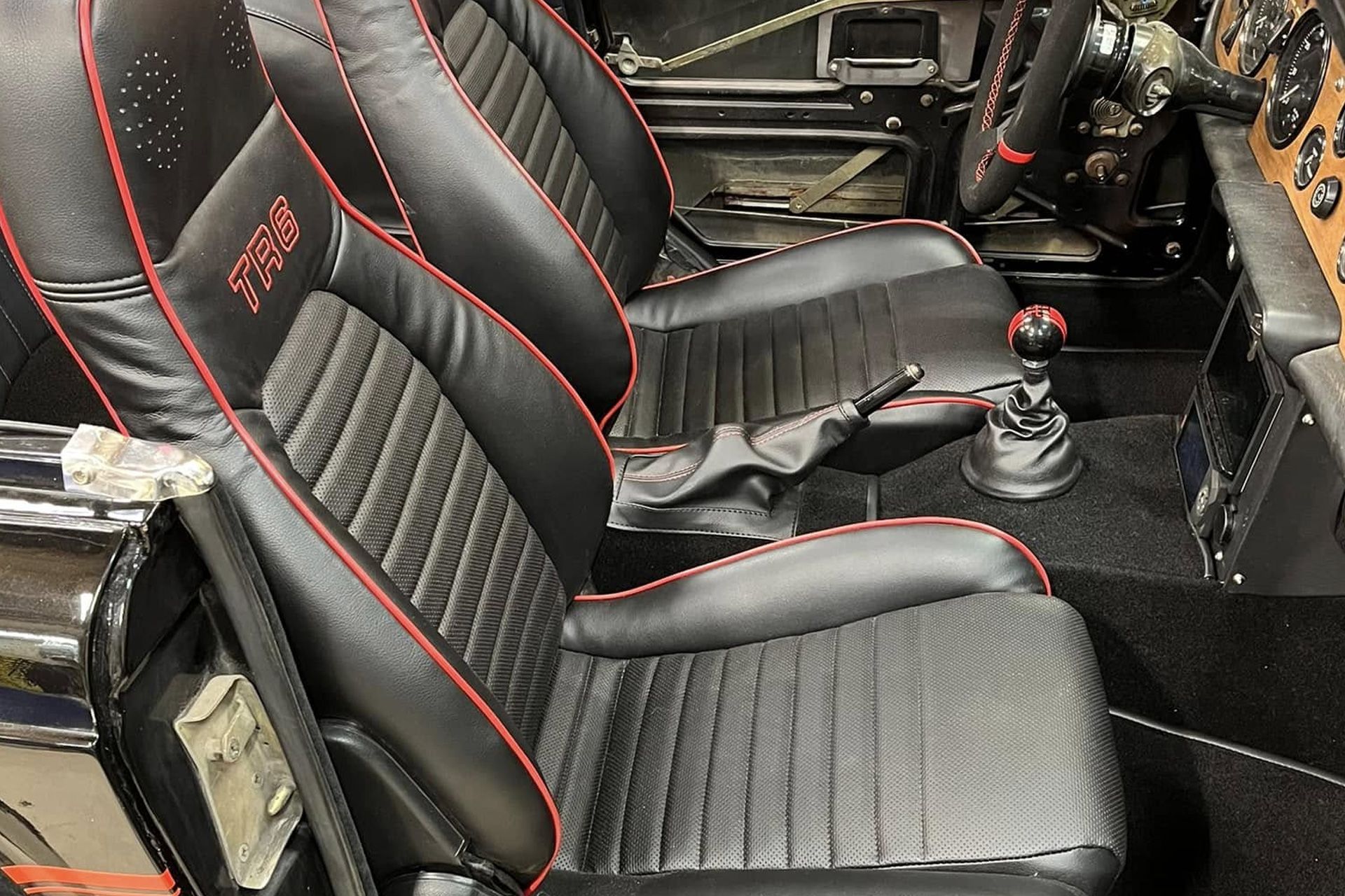 Two black racing bucket seats with red trim and stitched upholstery inside a car interior.