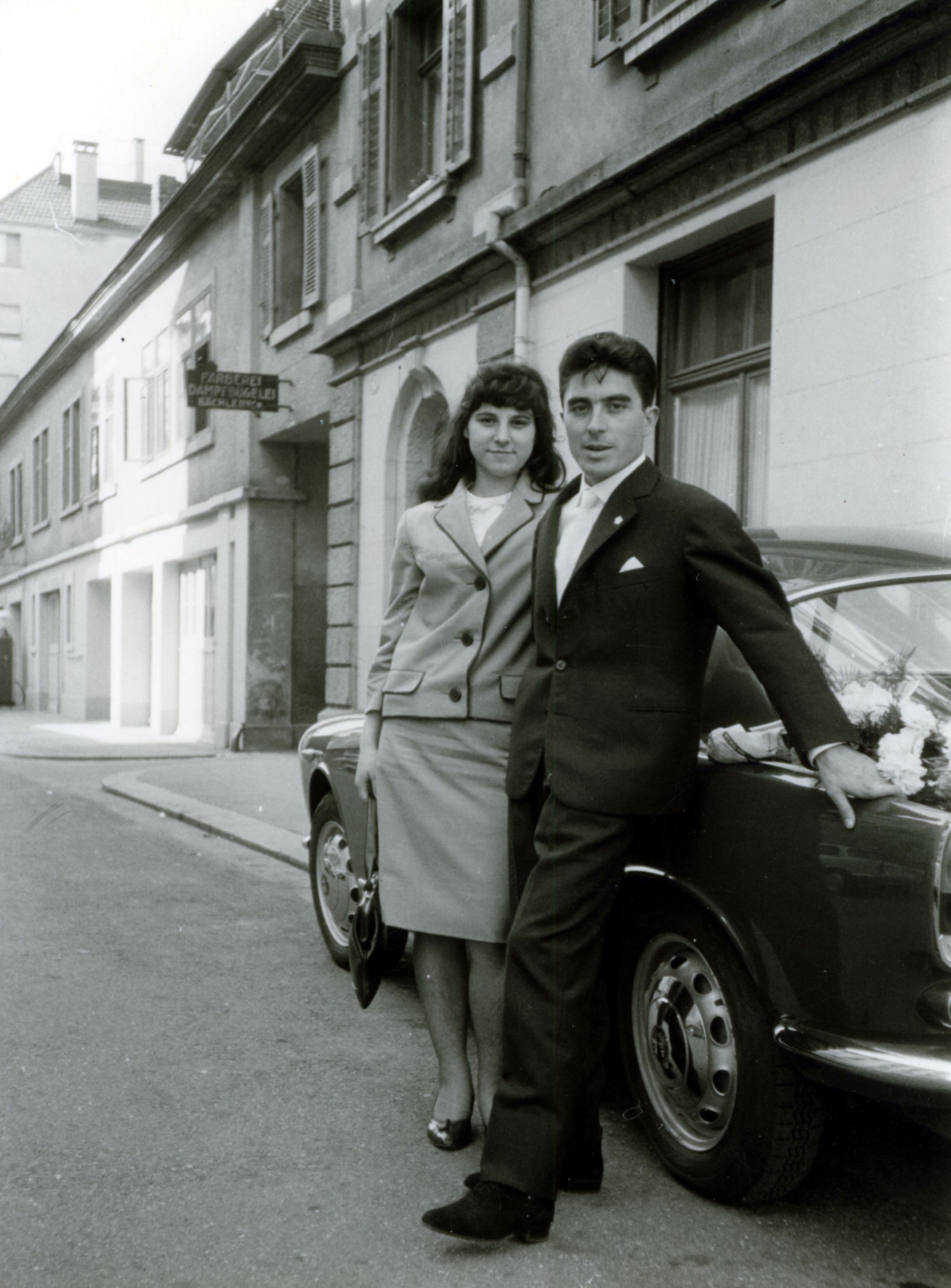 A black and white photo of a man and woman standing next to a car