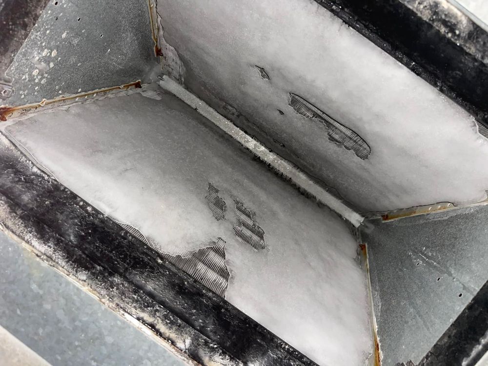 Close-up view of a dusty, rectangular metal duct interior, coated in a white substance.