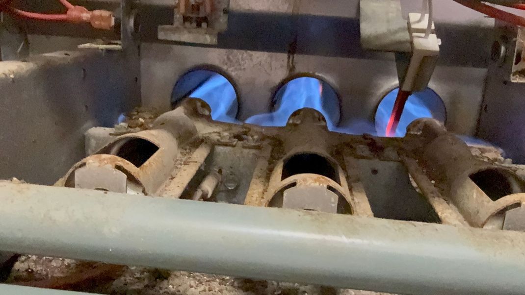 Close-up of blue gas flames burning in a metal industrial burner assembly