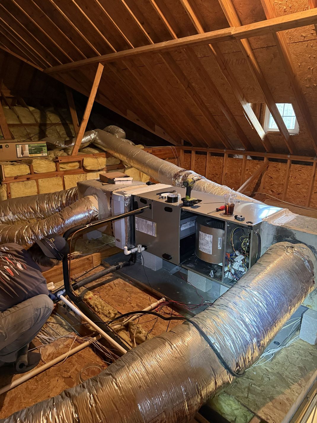 Attic with exposed roof beams, HVAC unit, and insulated ductwork under a sloped wooden ceiling