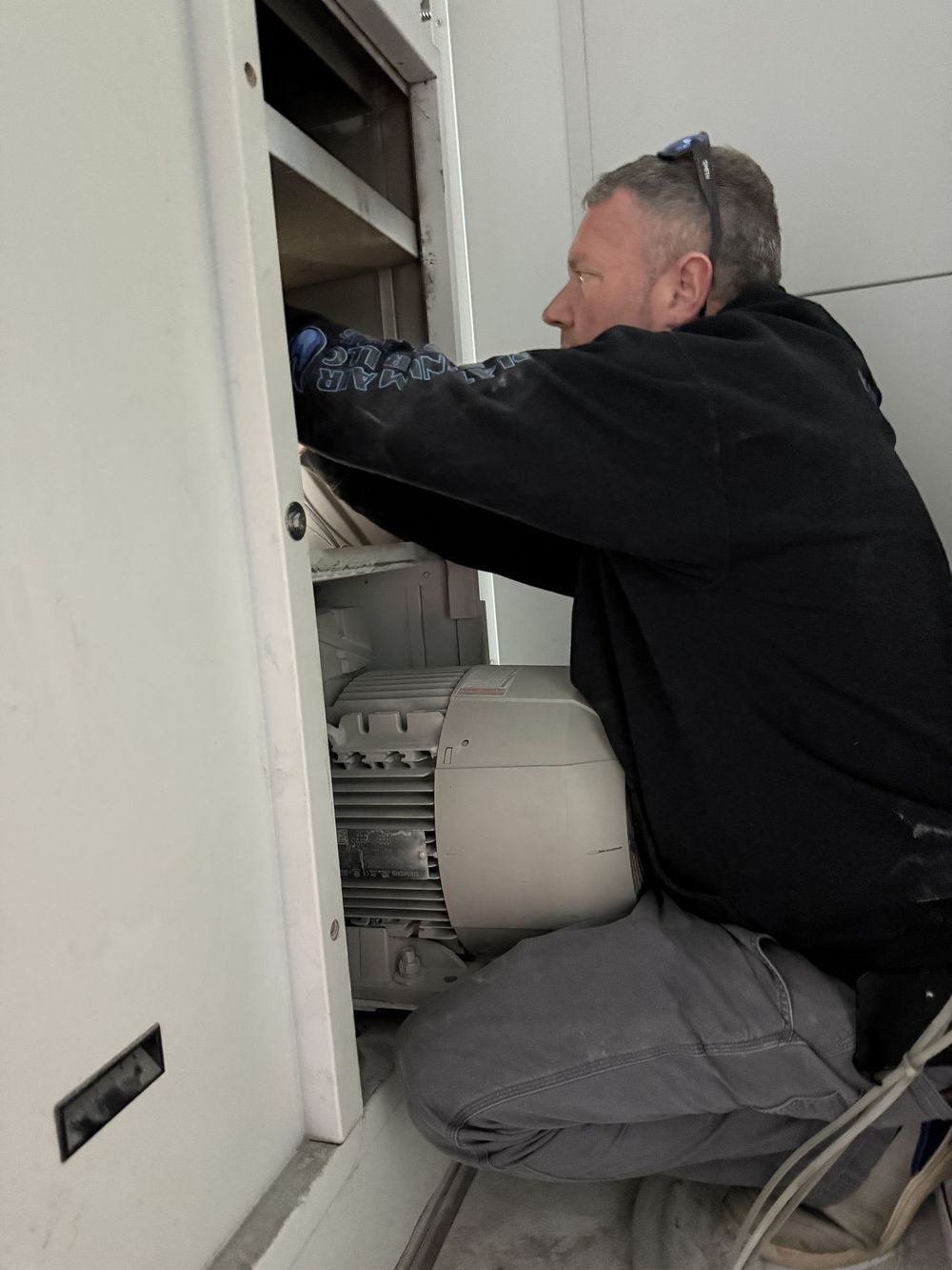Person kneeling in a cabinet, working on wiring or equipment inside a utility closet