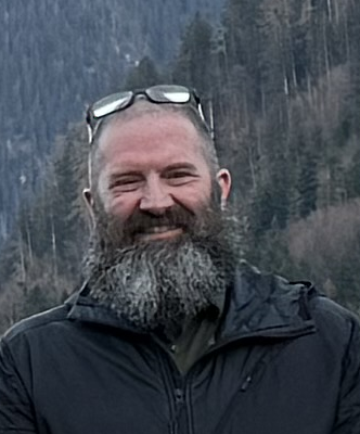 Ein Mann mit Brille und kariertem Hemd lächelt in die Kamera