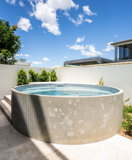 Circular concrete plunge pool outdoors with blue water, steps, and white wall under a blue sky.