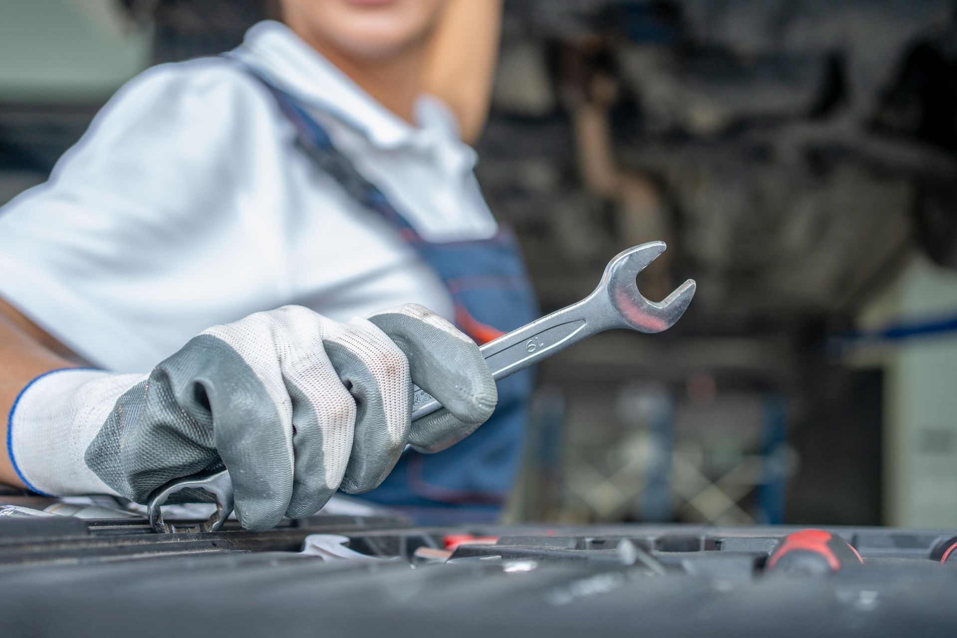 Mechanic in gray gloves using a wrench on a car engine in a repair shop