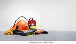 Casco de construcción, guantes, botiquín de primeros auxilios y botas de trabajo dispuestos sobre una superficie gris.