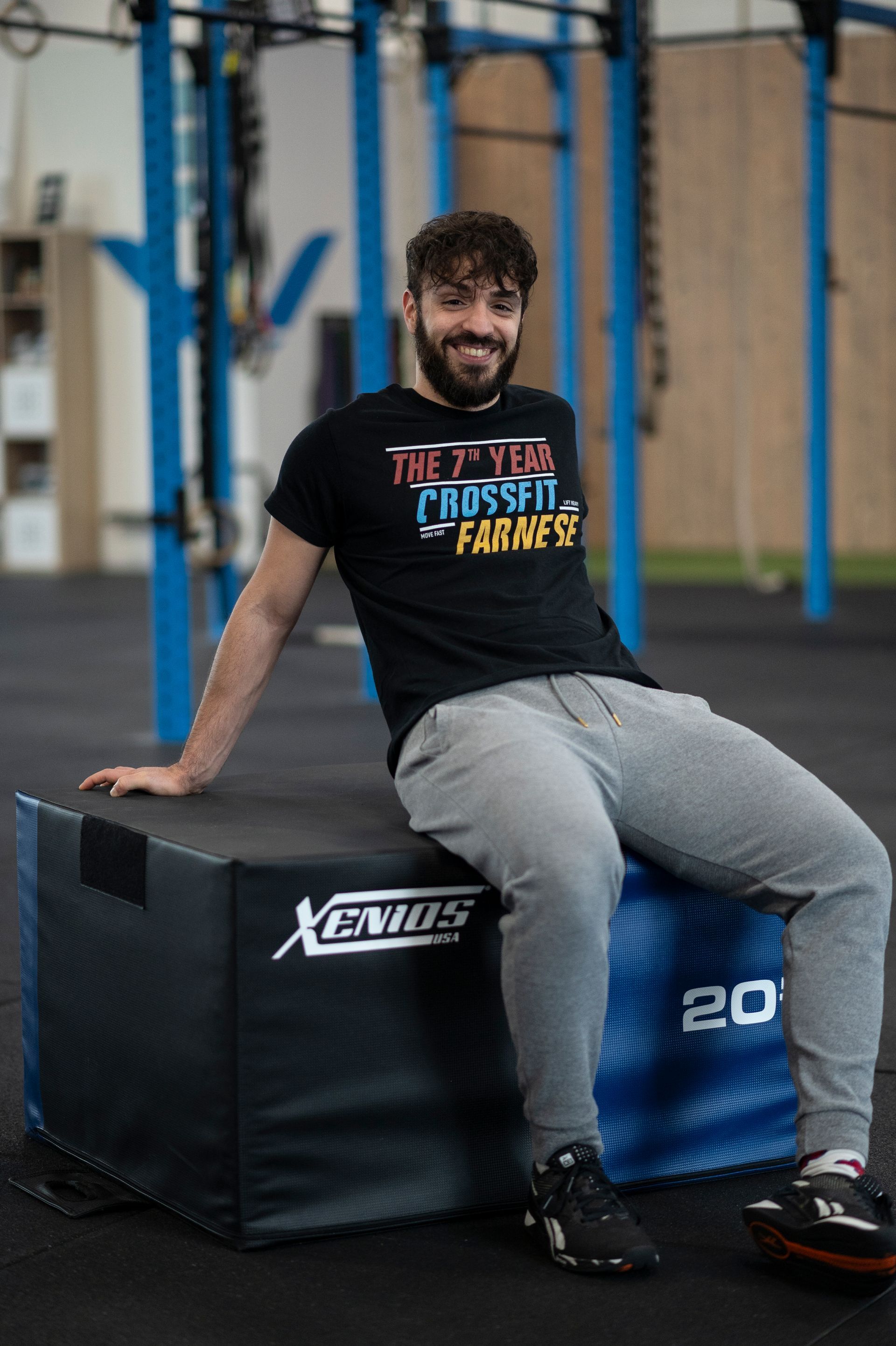 A man wearing a crossfit t-shirt is squatting down in a gym