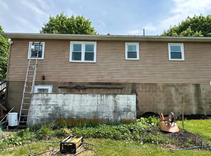 Back of a tan house with small windows, concrete foundation, and a ladder on the left side.