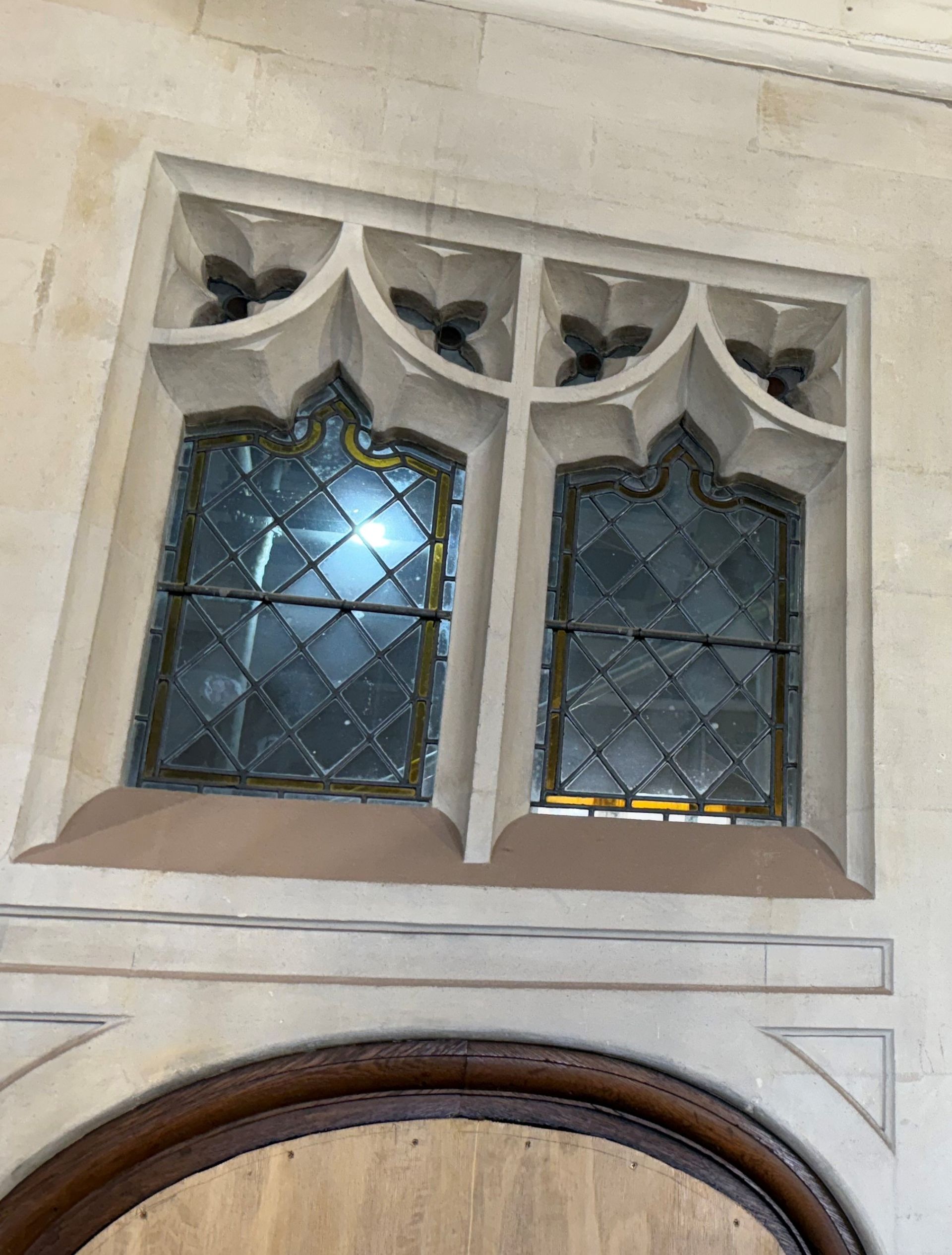A light stone wall featuring a window with two diamond-paned glass sections and decorative gothic tracery above.