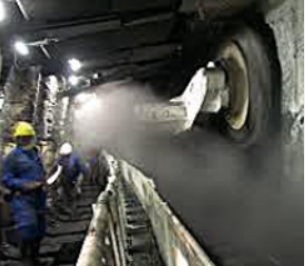 Two miners in hard hats and blue coveralls work inside a dusty, dimly lit tunnel with heavy mining equipment.