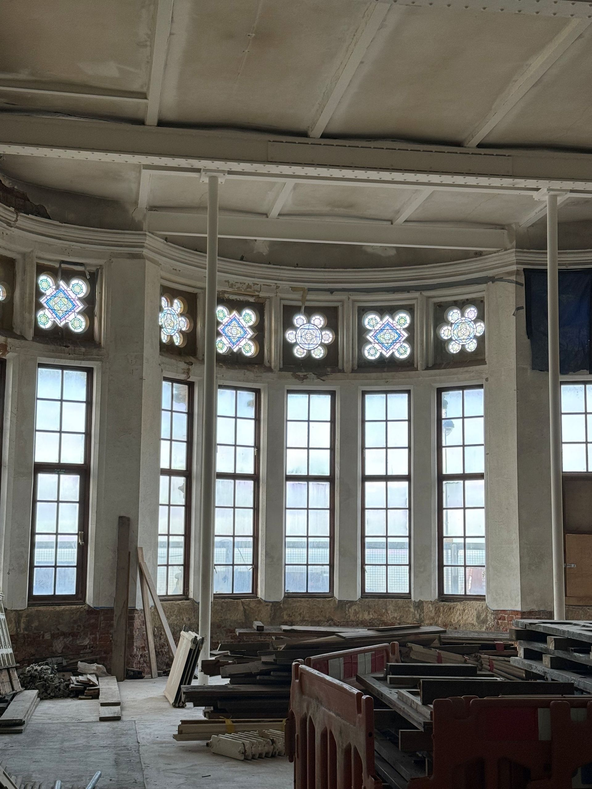 A semi-circular, unfinished room with tall grid windows topped by decorative patterned glass panels under construction.