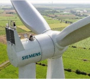Two technicians standing on top of a Siemens wind turbine nacelle with green fields in the background.