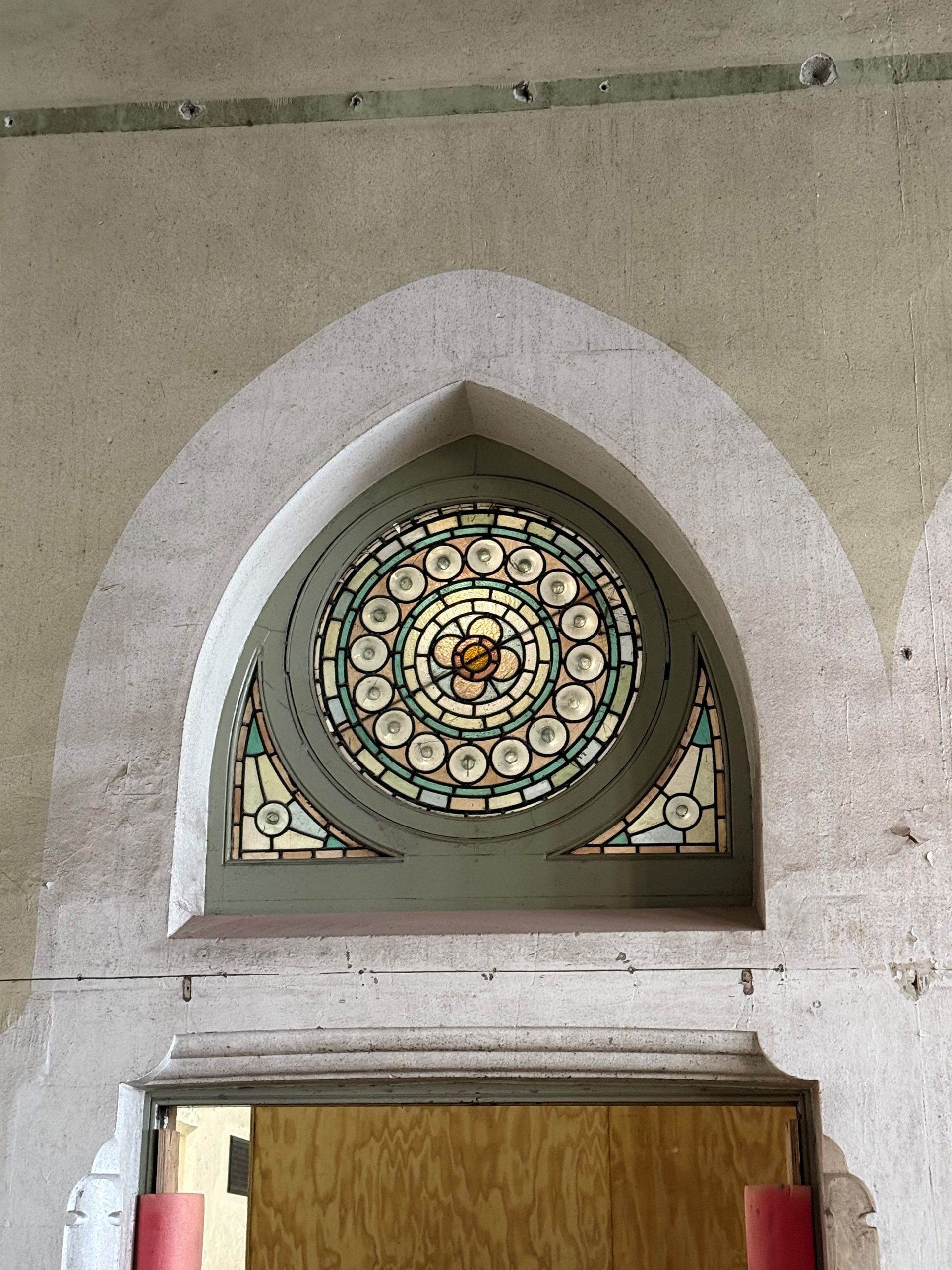 A decorative, circular stained-glass window set within a pointed stone arch above a wooden door.