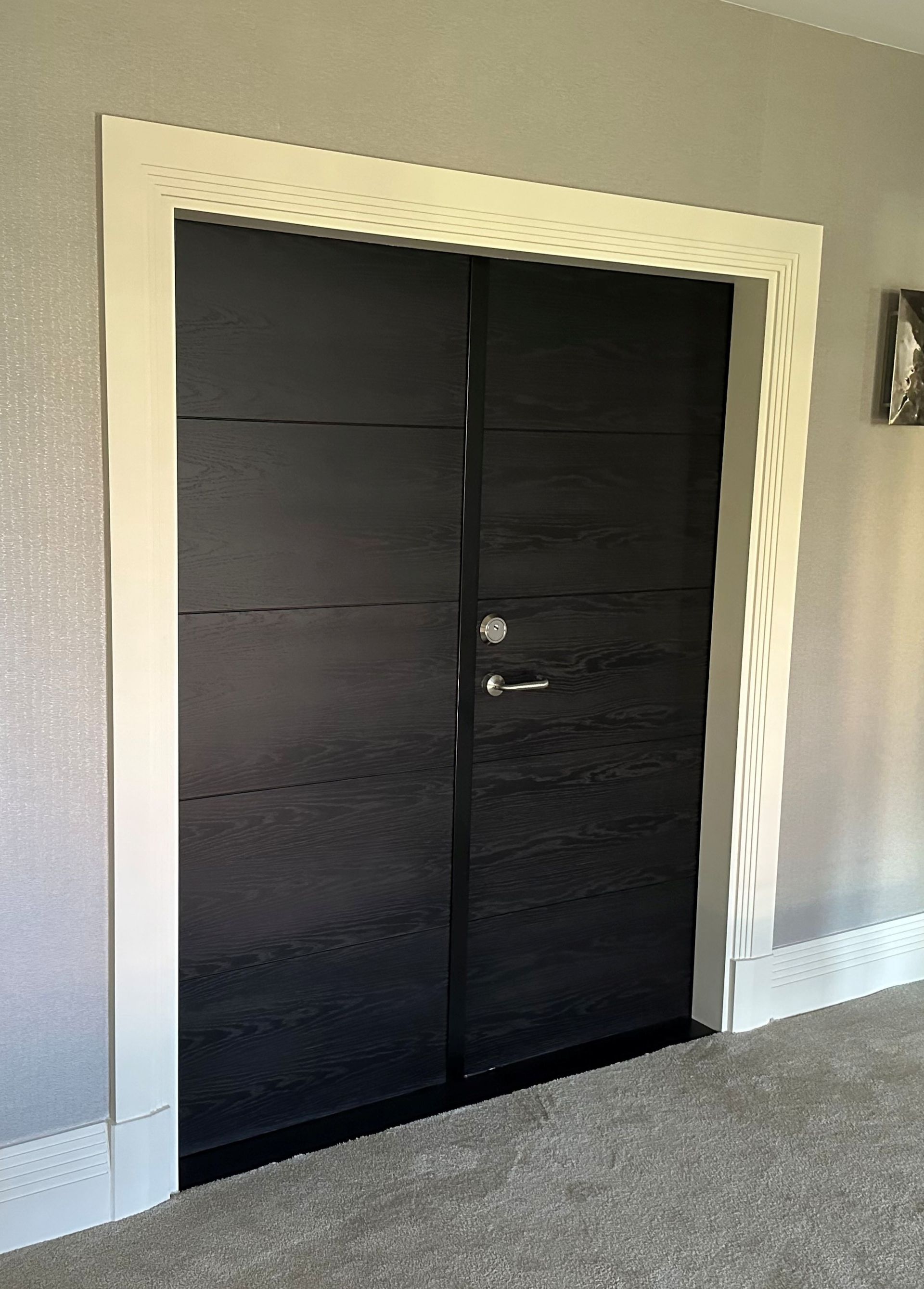 Double doors with a dark, textured horizontal-plank finish and silver hardware set in a wide white decorative door frame.