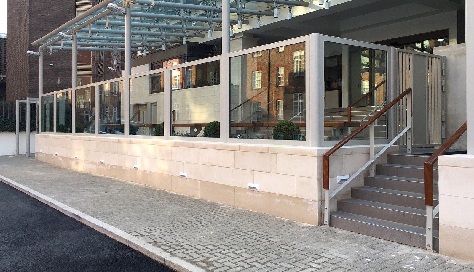 A raised outdoor terrace with a glass railing and covered roof, featuring a set of stairs leading to an entrance.