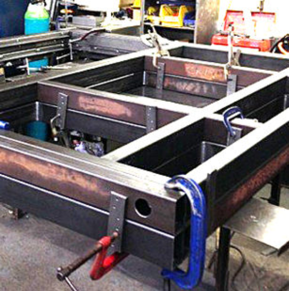Metal rectangular frame components clamped together on a workshop table for welding.