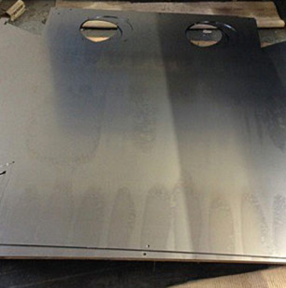 A rectangular metal sheet with two circular cutouts at the top, showing surface oxidation marks across the material.