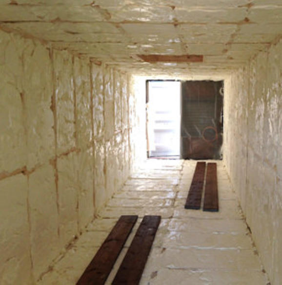 A rectangular space lined with light-colored insulation panels, with wooden planks on the floor leading toward a doorway.