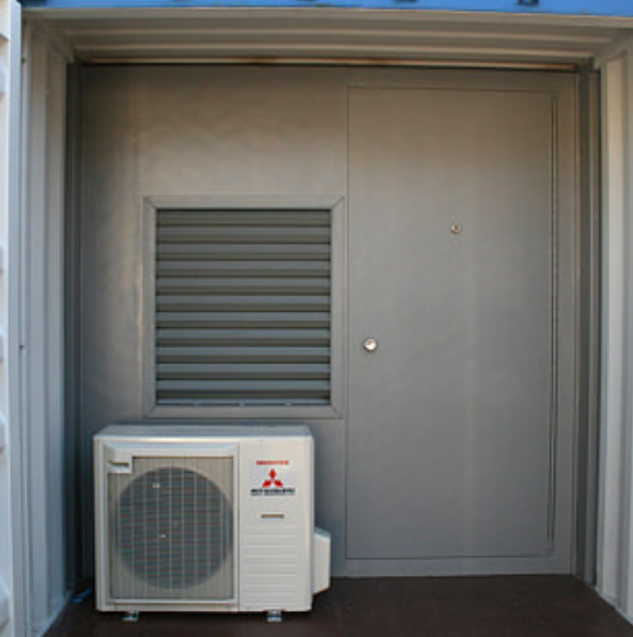 A grey door with an adjacent ventilation grille and a white Mitsubishi air conditioning unit in a shipping container.