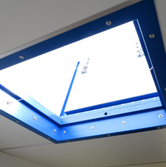 A low-angle view of a rectangular skylight set in a white ceiling, framed by a bright blue, bolt-fastened border.