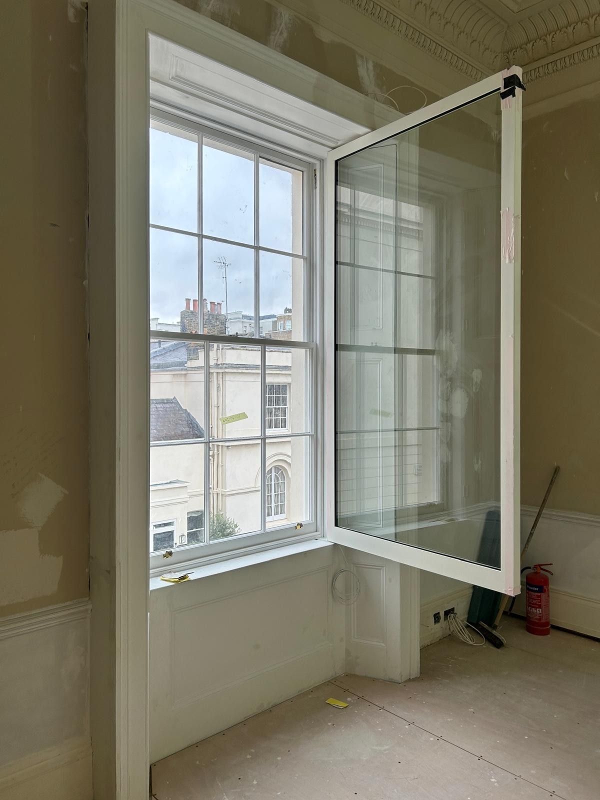 A white window frame is open in a room with light-colored walls, revealing a view of neighboring buildings outside.