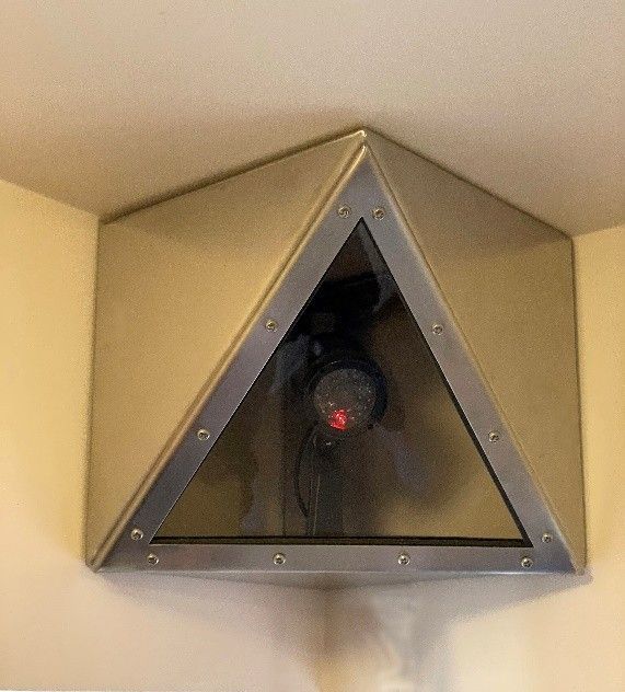 A security camera encased in a triangular, metallic housing mounted in the corner of a room.