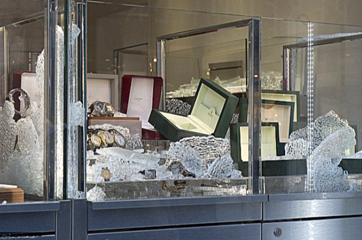 Shattered glass display cases in a jewelry store with empty watch boxes visible inside.