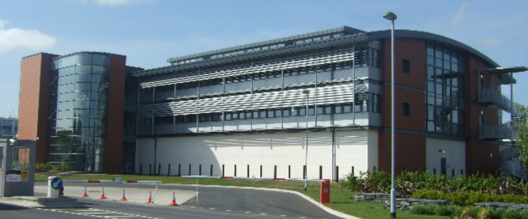 A multi-story building featuring red brick, glass facades, and metal window shades under a blue sky.