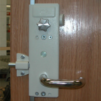 A light-colored surface-mounted door lock with a horizontal lever handle and a star-shaped thumbturn on a wood door.