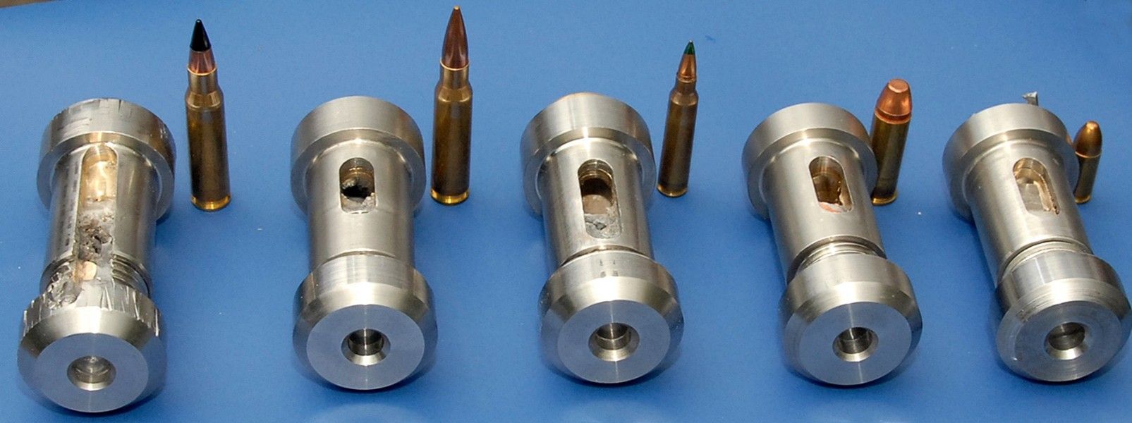 A lab technician assembles small, metallic, cylindrical devices shown alongside various bullet casings on a blue surface.