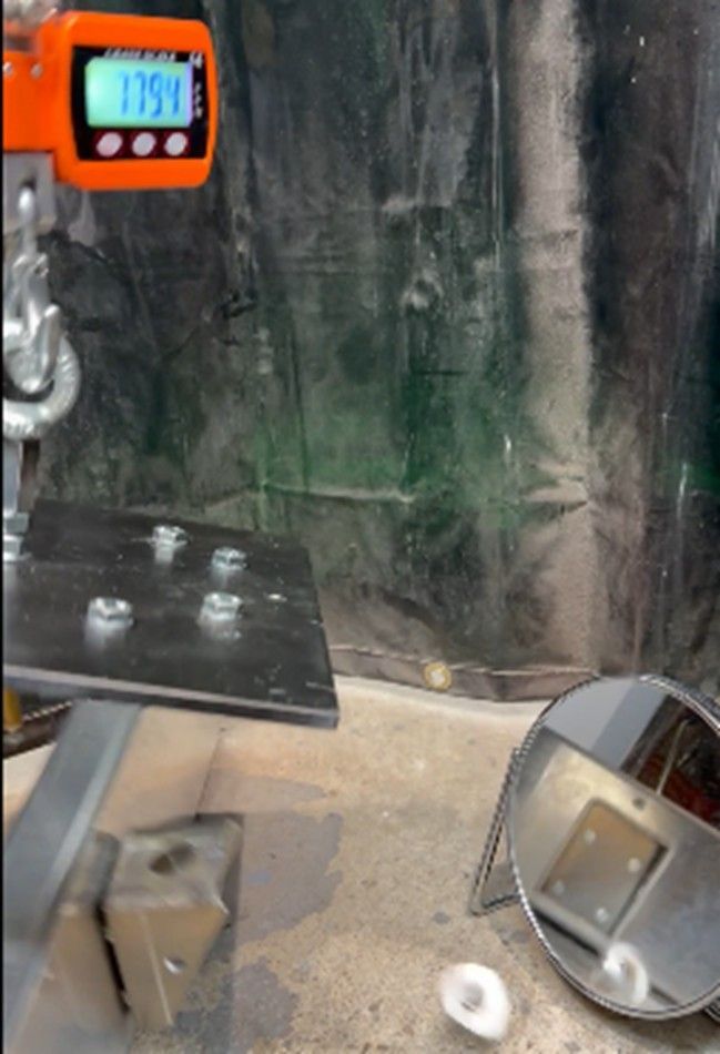A digital crane scale displays 175.4 above a metal plate with four bolts, while a round mirror reflects the setup below.