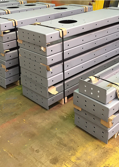 Stacked grey industrial steel beams with circular cutouts, secured by straps on wooden pallets in a warehouse.