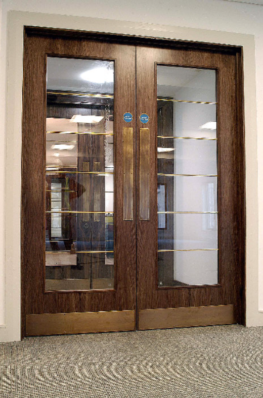 Double wood-grain doors with vertical glass panels and gold handles, installed in an office entryway with carpet.